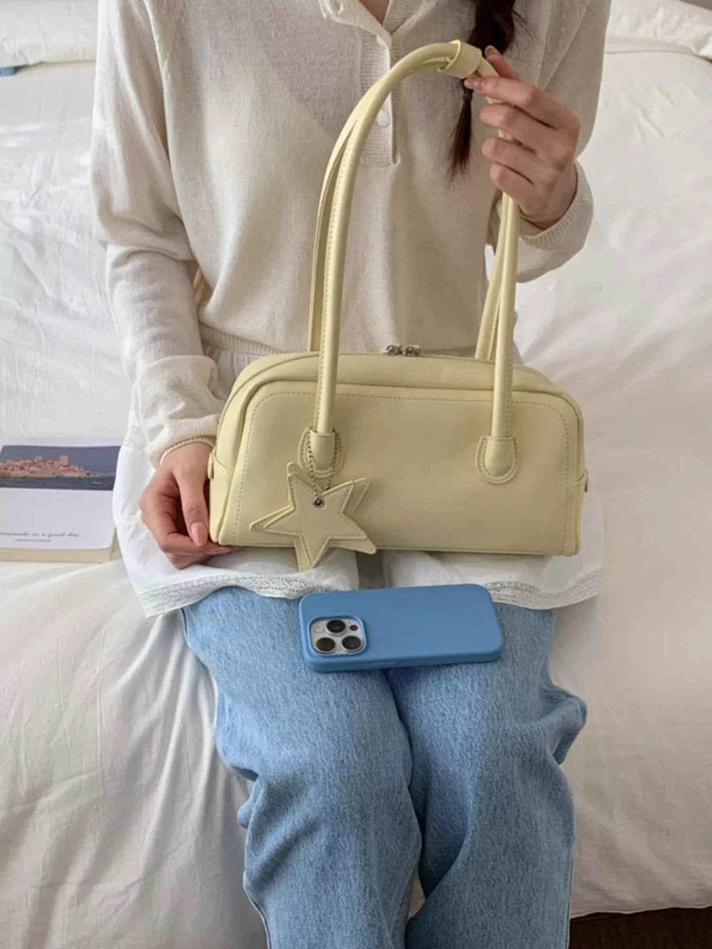 Cream bowler bag with star charm, held by woman in cozy outfit, perfect for trendy fashion accessories.