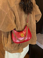 Red crescent-shaped shoulder bag with gold chain strap, worn with brown jacket