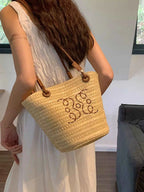Straw tote bag with embroidered design, carried by woman in white dress, summer fashion accessory