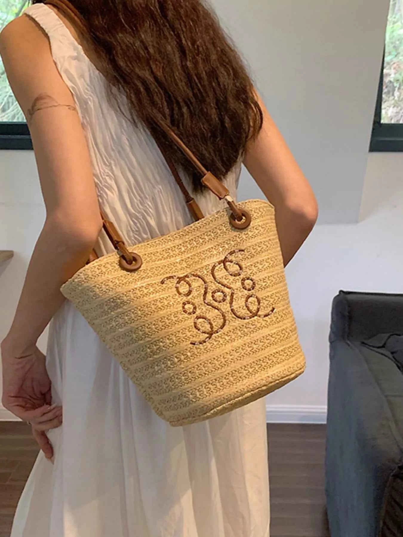 Straw tote bag with embroidered design, carried by woman in white dress, summer fashion accessory