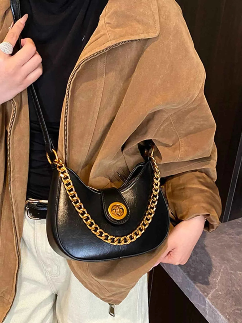 Black crescent moon bag with gold chain strap, worn with brown jacket and black top