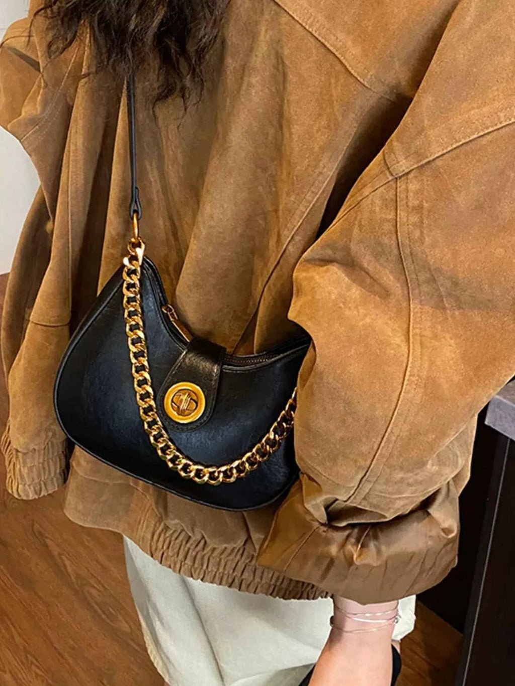 Stylish black crescent bag with gold chain strap, worn over brown jacket for chic everyday look