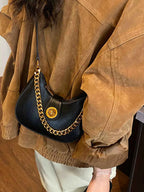 Stylish black crescent bag with gold chain strap, worn over brown jacket for chic everyday look
