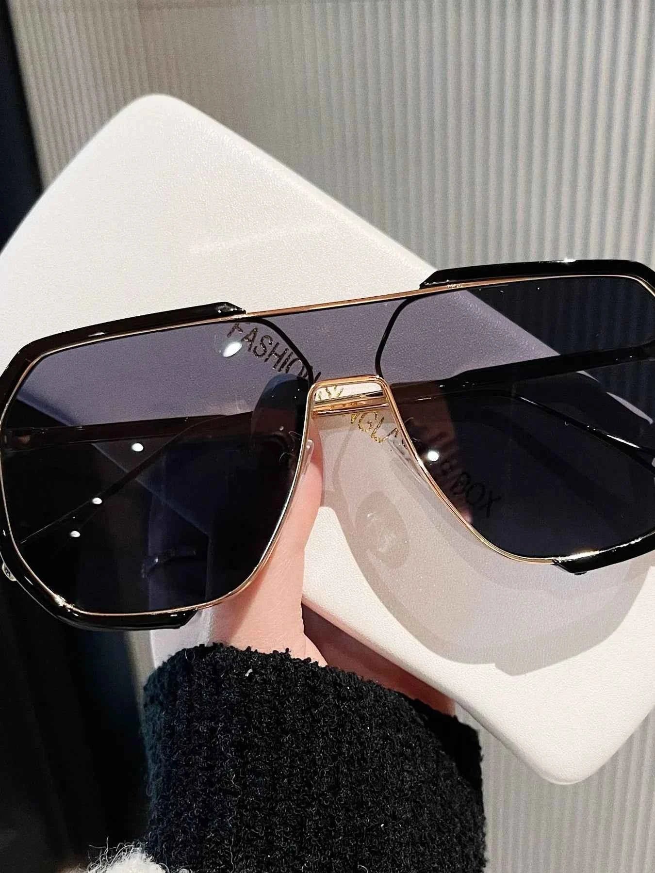 Stylish oversized sunglasses with gold trim, held against a white case, perfect for fashion-forward looks.