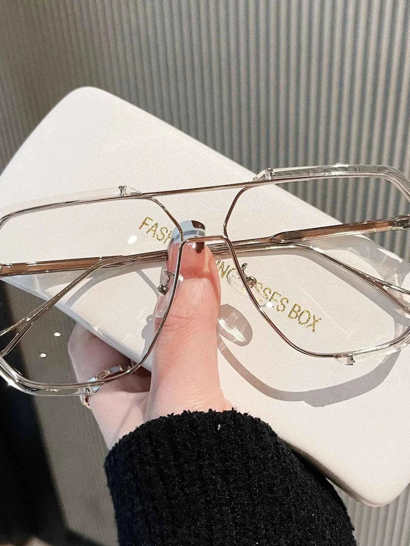 Trendy clear frame sunglasses with gold accents, held over a white 'FASHION EYES BOX' case.