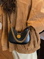 Black crescent moon bag with gold chain strap, worn over brown jacket, stylish fashion accessory