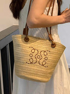 Straw tote bag with monogram embroidery, brown leather straps, perfect for summer fashion and beach outings.