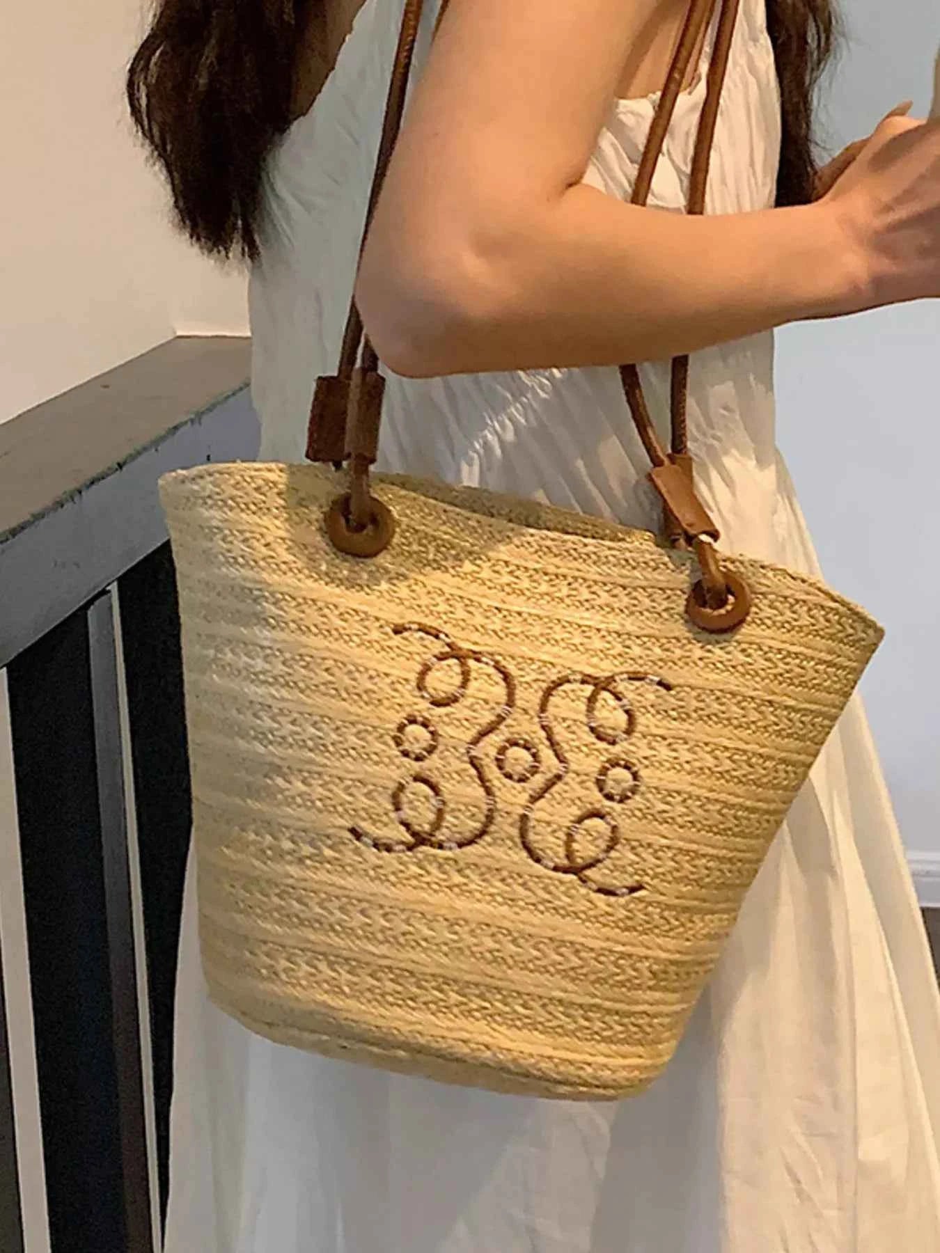 Straw tote bag with monogram embroidery, brown leather straps, perfect for summer fashion and beach outings.