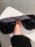 Stylish oversized aviator sunglasses with gold frame and dark lenses, held against white bag