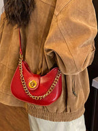 Red crescent-shaped crossbody bag with gold chain strap, worn with brown jacket