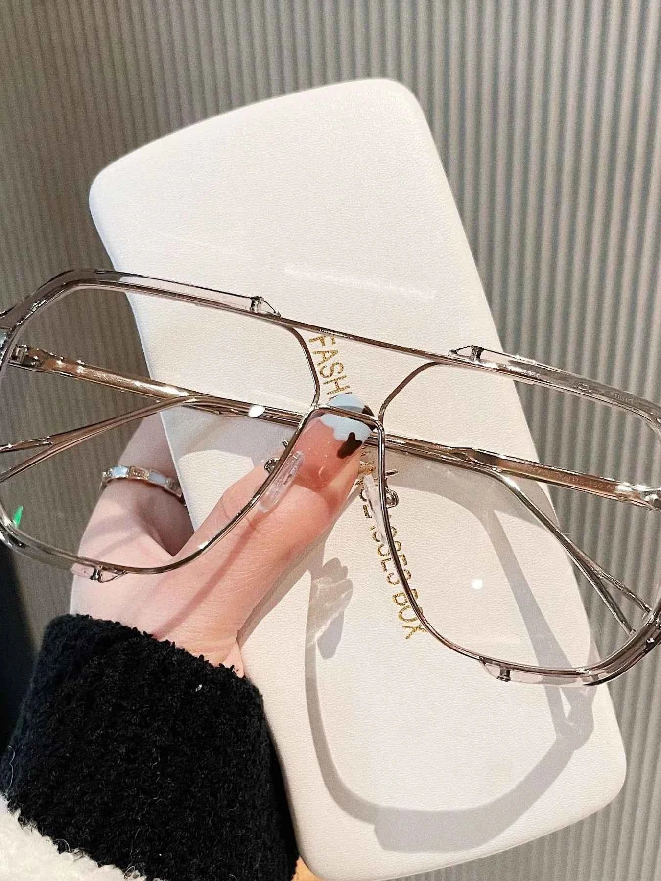 Trendy oversized clear frame glasses with gold accents, held over a white case, perfect for fashion accessories.