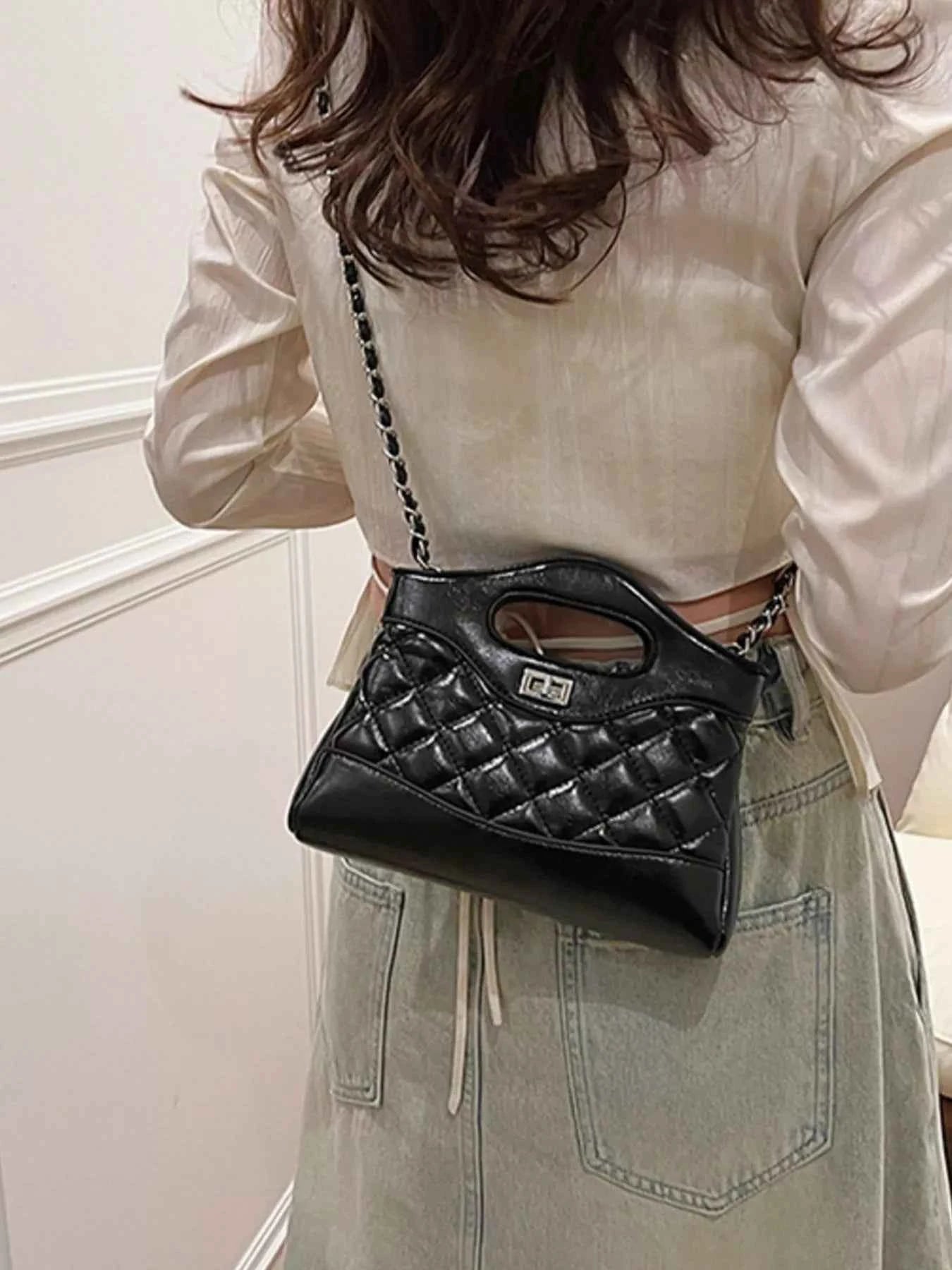 Black quilted crossbody bag with chain strap and top handle, worn with white blouse and denim skirt.