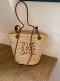Straw bucket bag with beaded monogram, brown leather straps, perfect for summer fashion accessories.