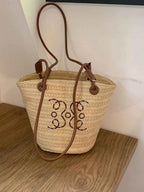 Straw bucket bag with beaded monogram, brown leather straps, perfect for summer fashion accessories.