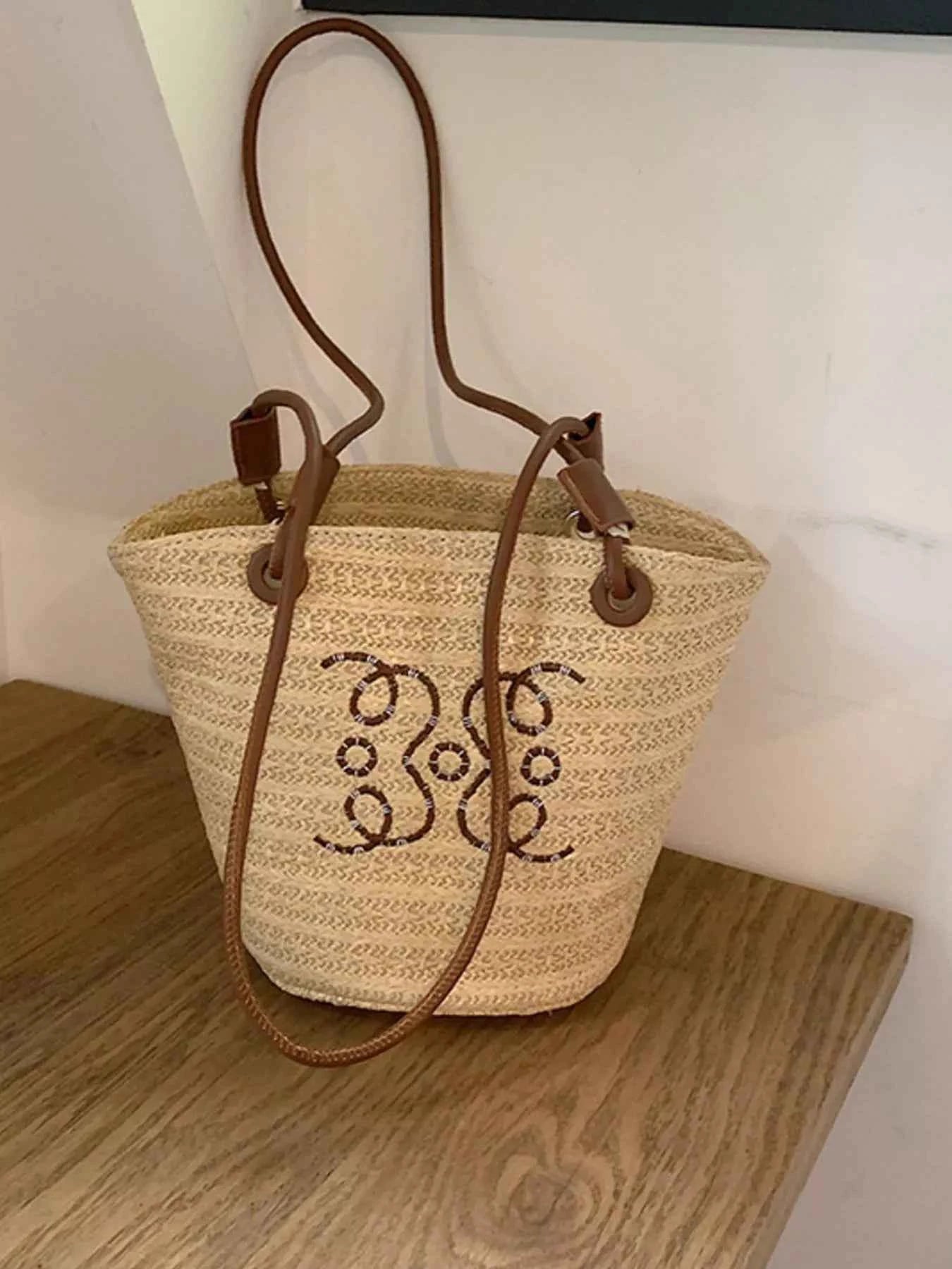 Straw bucket bag with beaded monogram, brown leather straps, perfect for summer fashion accessories.