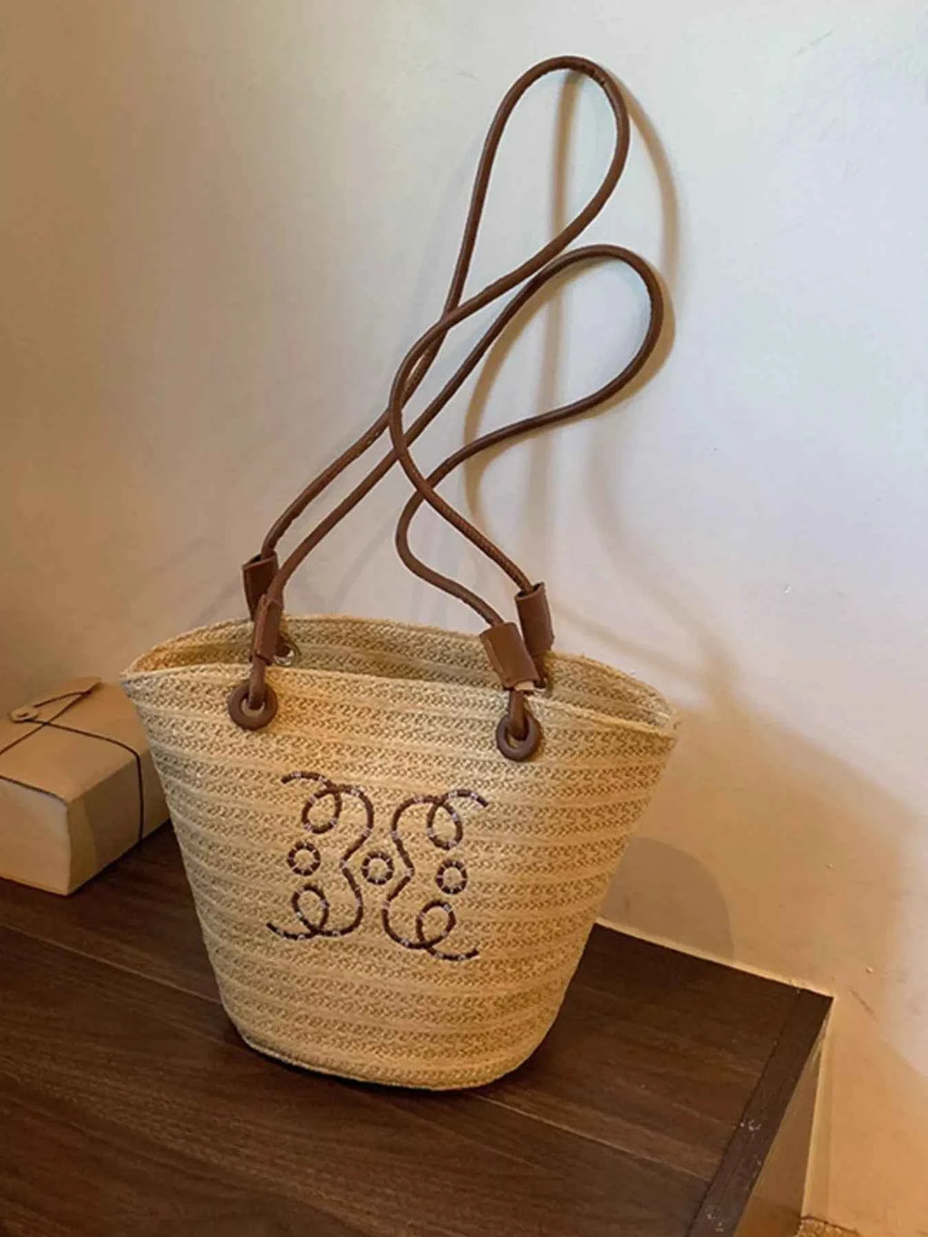Woven straw tote bag with brown leather handles and monogram embroidery, stylish summer accessory